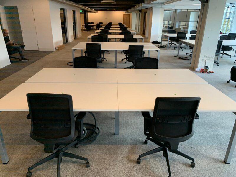 Modern open-plan office fit-out for CTI Digital in Manchester featuring integrated white bench desks and ergonomic black office chairs.