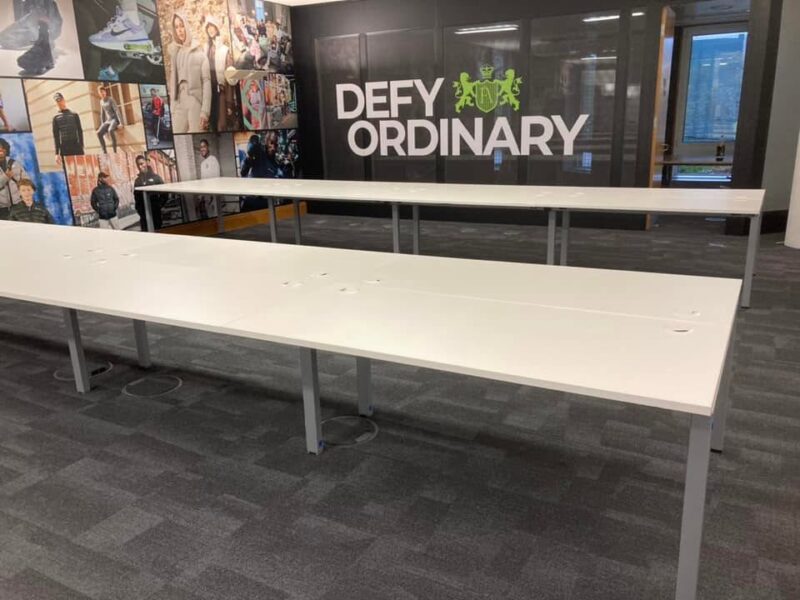 Close up detail of a clean white desktop surface, white steel bench frame, and black task chair.